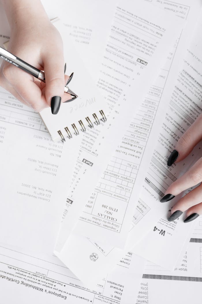Close-up of hands writing notes on a notepad over tax forms, showcasing financial planning.